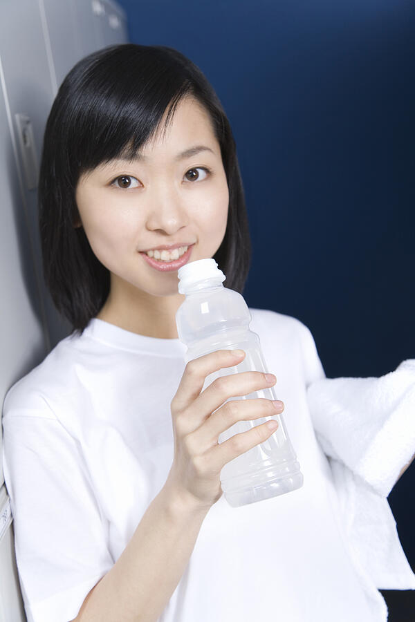 Portrait of a teenage girl in gym cloth smiling and holding a bottle of water in locker room Photograph by Daj