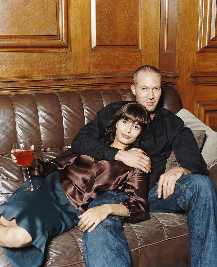 Portrait of a Twentysomething Couple Sitting on a Leather Sofa with the Woman Holding a Glass of Red Wine Photograph by A J James