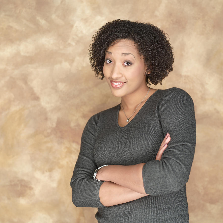 Portrait Of A Young African American Woman In A Grey Sweater As She Folds Her Arms And Smiles Photograph by Photodisc
