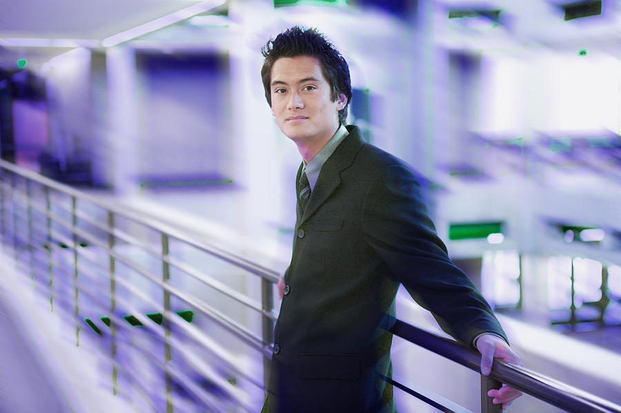 Portrait Of A Young Asian Business Man In A Dark Suit As He Laens Against A Railing Photograph by Photodisc