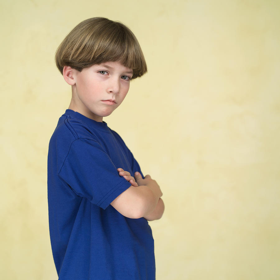 Portrait Of A Young Caucasian Boy In A Blue Shirt As He Folds His Arms And Tries To Look Tough Photograph by Photodisc