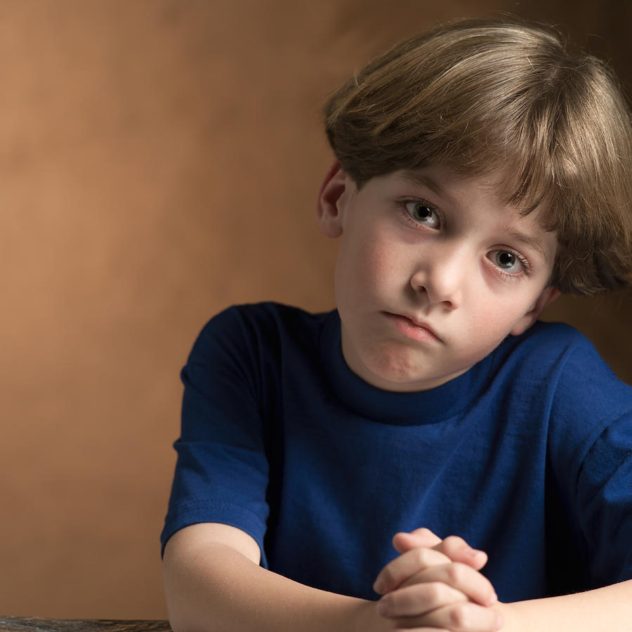 Portrait Of A Young Caucasian Boy In A Blue Shirt As He Makes A Sad Face Photograph by Photodisc