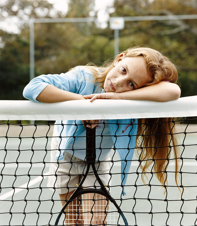 Portrait of a Young Girl Leaning on a Net in a Tennis Court Photograph by Digital Vision.