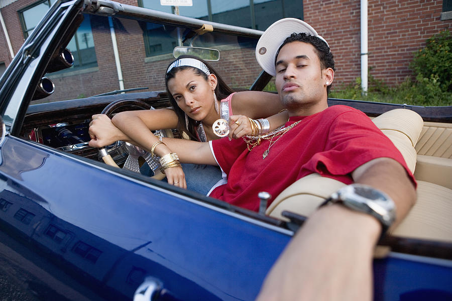 Portrait of a young hip-hop couple sitting in a pimped-up vintage car Photograph by Purestock