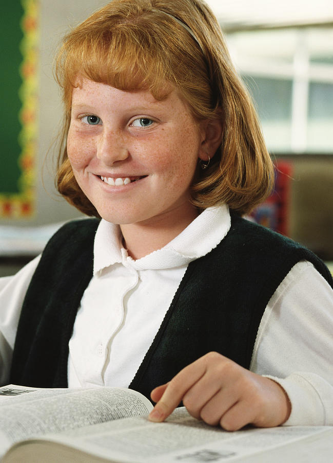 Portrait Of A Young Redheaded Girl As She Sits And Smiles At Her Desk In Her Classroom Photograph by Photodisc