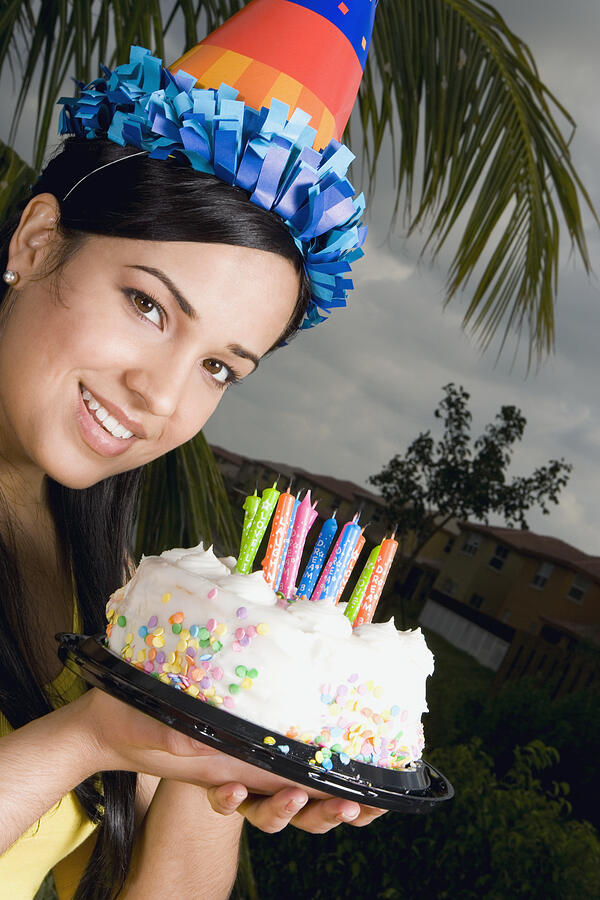 Portrait of a young woman holding a birthday cake and smiling Photograph by Glowimages