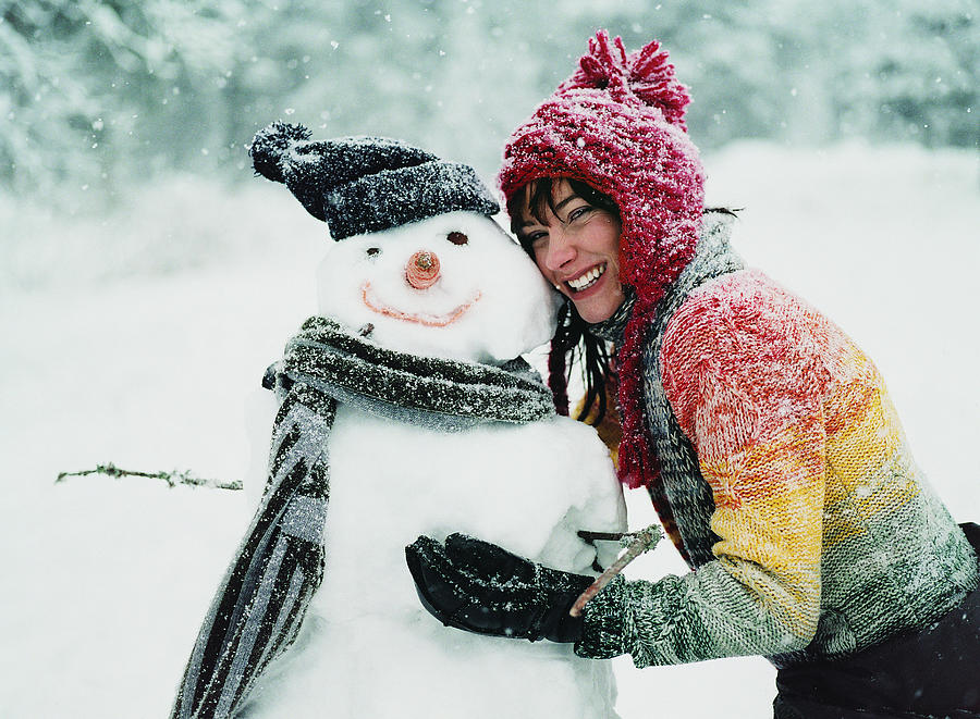 Portrait of a Young Woman in the Snow Next to a Snowman Photograph by Digital Vision.