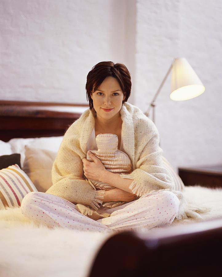Portrait of a Young Woman Sitting on a Bed and Holding a Hot Water Bottle Photograph by Digital Vision.