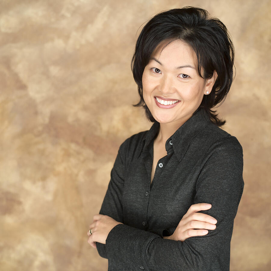Portrait Of An Asian Woman In A Black Shirt As She Folds Her Arms As She Looks Into The Camera Photograph by Photodisc