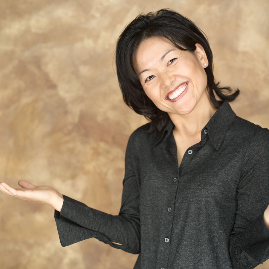Portrait Of An Attractive Asian Woman In A Black Shirt As She Gestures With Her Arm And Smiles Photograph by Photodisc