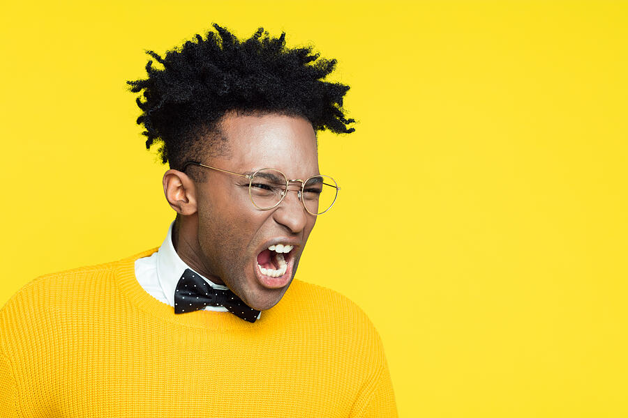 Portrait of angry nerdy young man screaming against yellow background Photograph by Izusek
