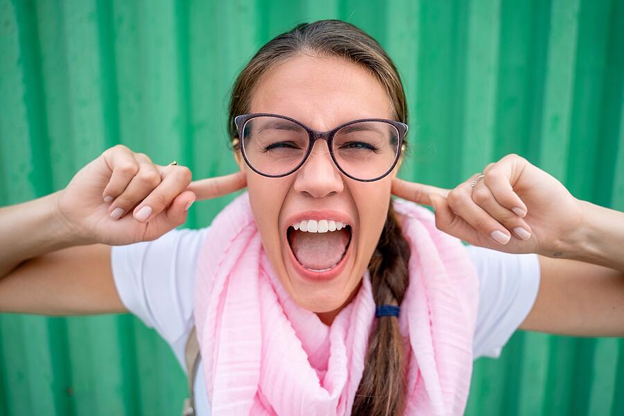 Portrait of Beautiful Woman Screaming with Fingers in Ears against Green Background - stock photo Photograph by CasarsaGuru