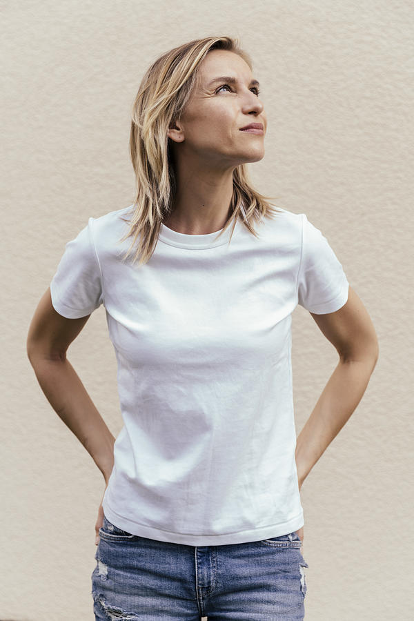 Portrait of blond woman wearing white t-shirt in front of light wall looking up Photograph by Westend61