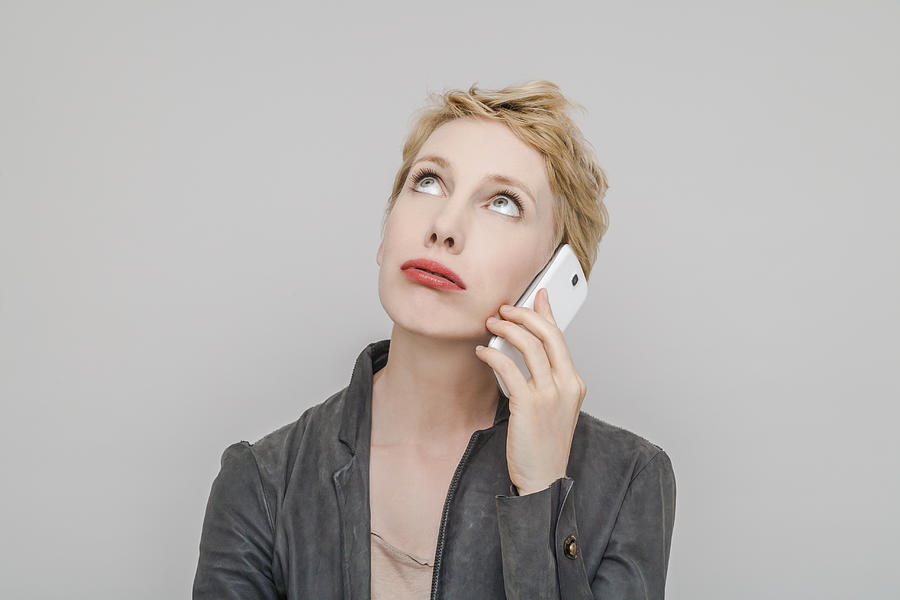 Portrait of blond woman with smartphone pouting mouth looking up Photograph by Westend61
