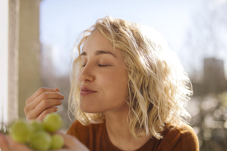 Portrait of blond young woman eating green grapes Photograph by Westend61