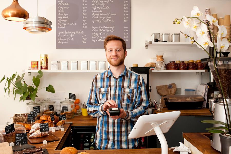 Portrait of cafe waiter with card machine behind counter Photograph by Rogan Macdonald