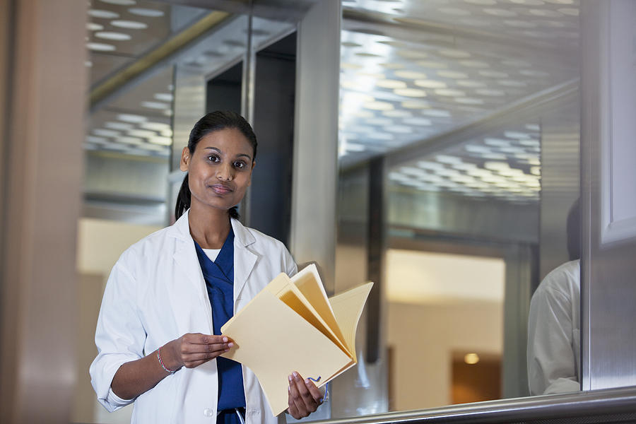 Portrait of confident doctor holding medical record in hospital elevator Photograph by Sam Edwards