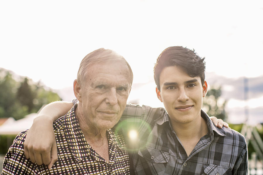 Portrait of confident grandfather and grandson with arms around against sky Photograph by Maskot