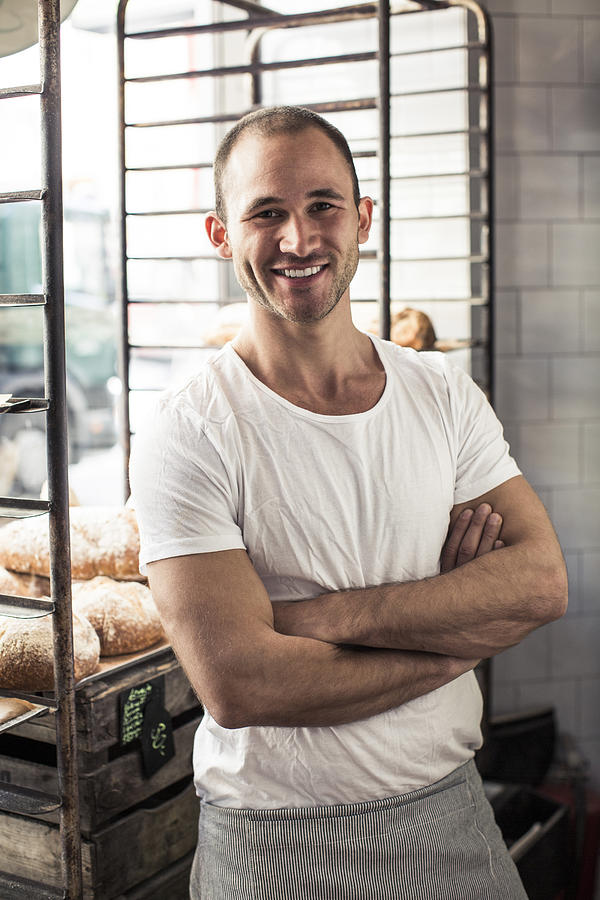Portrait of confident male owner standing arms crossed in bakery Photograph by Maskot