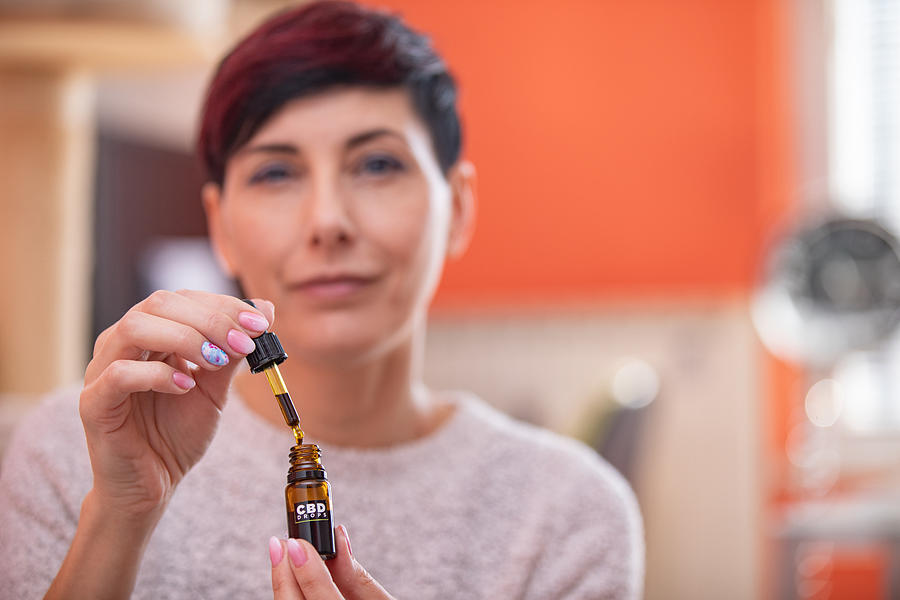 Portrait of Content Adult Woman Holding CBD Oil Drops in Domestic Room Photograph by CasarsaGuru