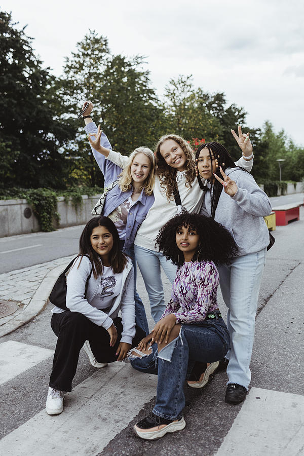 Portrait of female friends gesturing with peace sign on street Photograph by Maskot