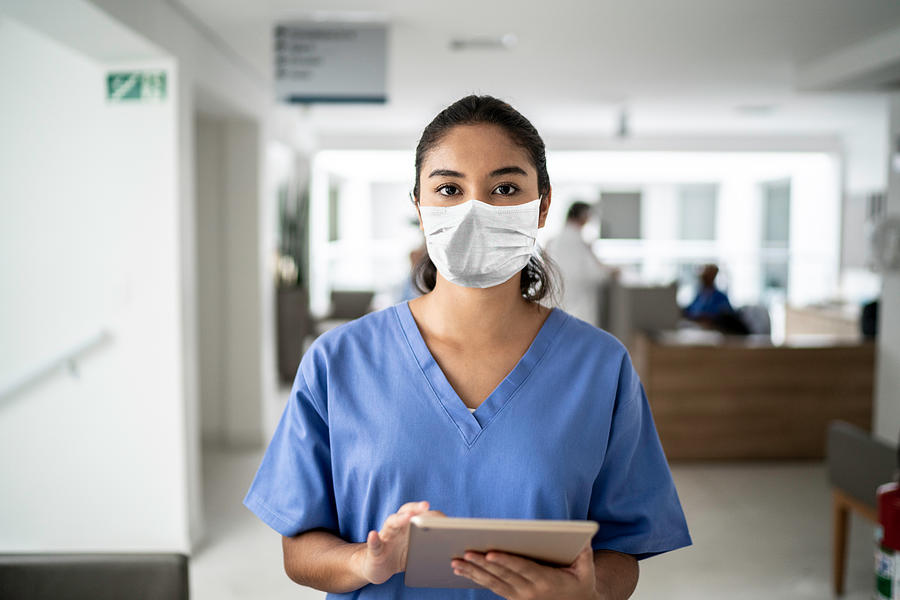 Portrait of female nurse holding digital tablet at hospital using protective mask Photograph by FG Trade