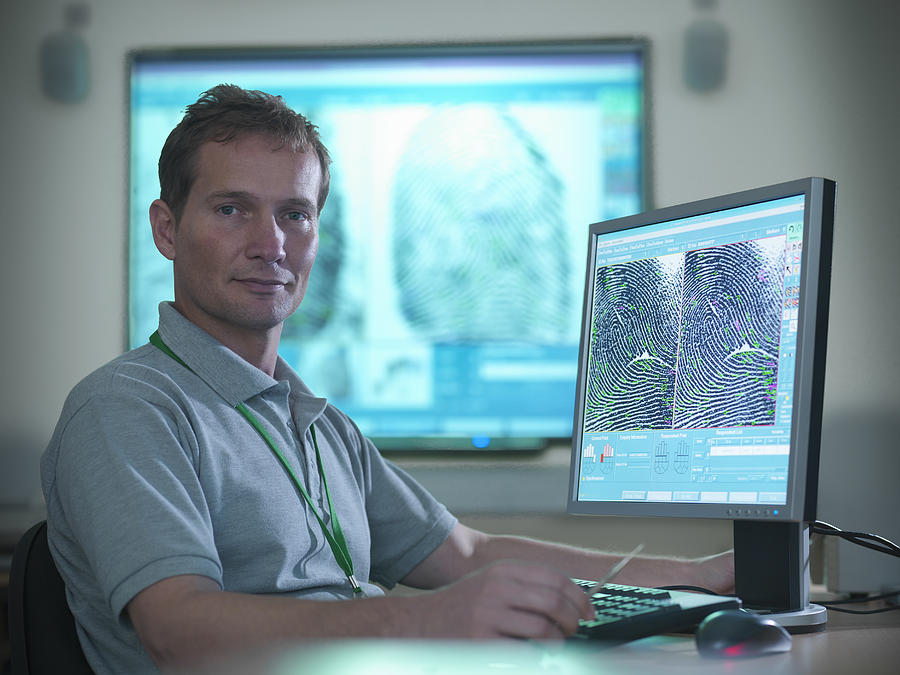 Portrait of forensic scientist at desk with fingerprints on screen in laboratory Photograph by Monty Rakusen