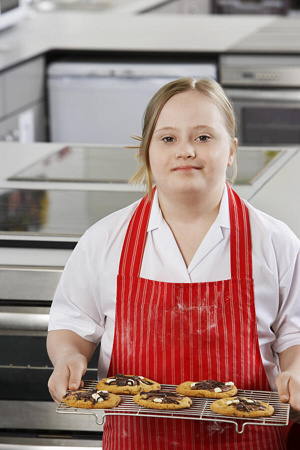 Portrait of girl (10-12) with Down syndrome carrying cookies on baking sheet Photograph by Moodboard