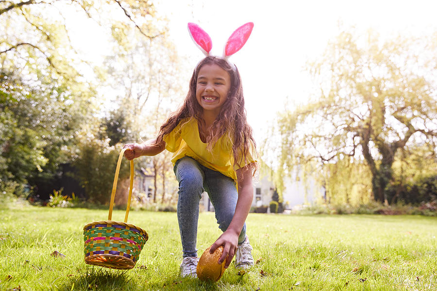 Portrait Of Girl Wearing Bunny Ears Finding Chocolate Egg On Easter Egg Hunt In Garden Photograph by Monkeybusinessimages