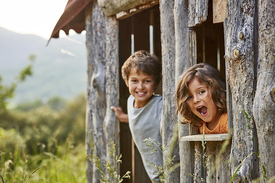 Portrait of happy siblings playing in log cabin Photograph by Morsa Images