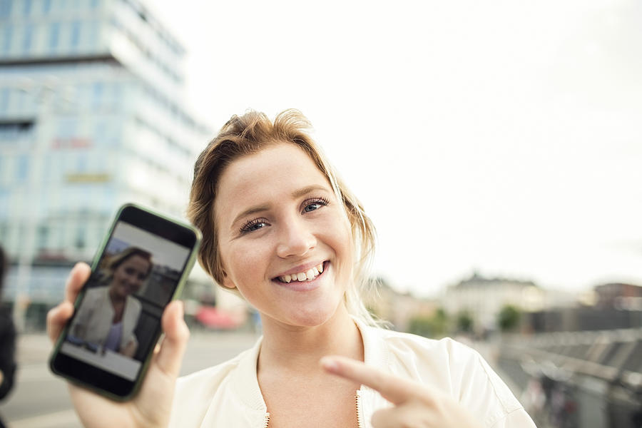 Portrait of happy woman showing photograph in mobile phone Photograph by Maskot