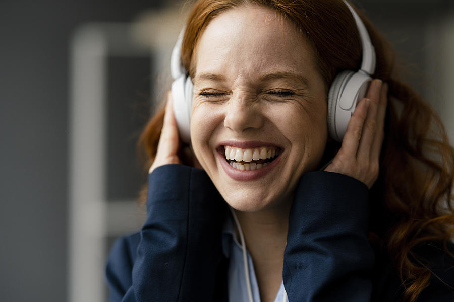 Portrait of laughing redheaded businesswoman listening music with white headphones Photograph by Westend61