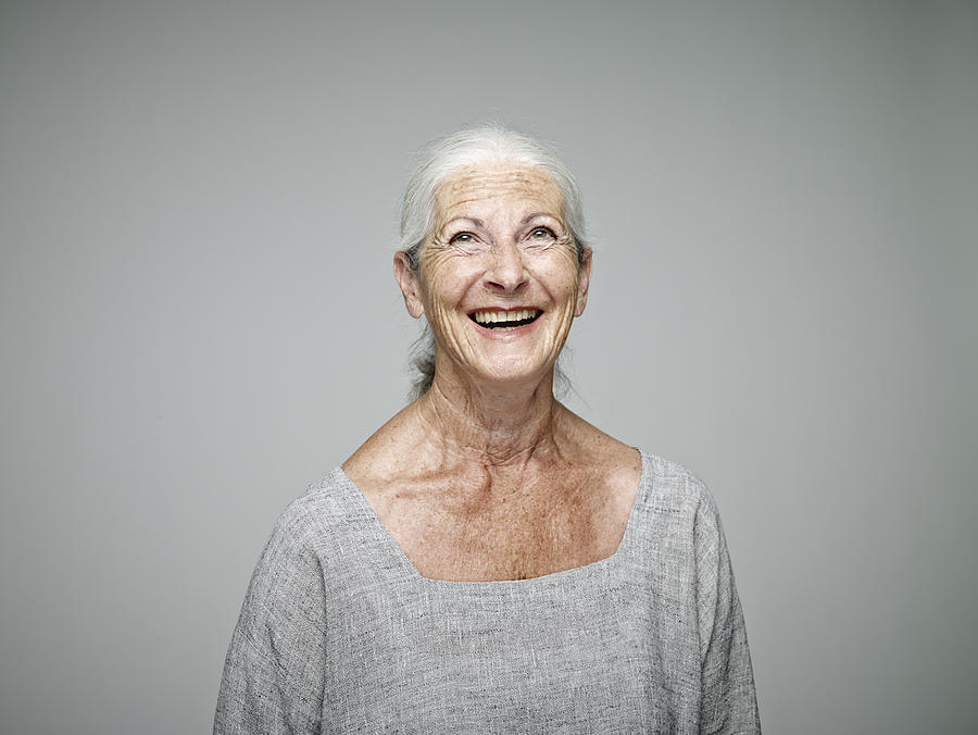 Portrait of laughing senior woman looking up in front of grey background Photograph by Westend61