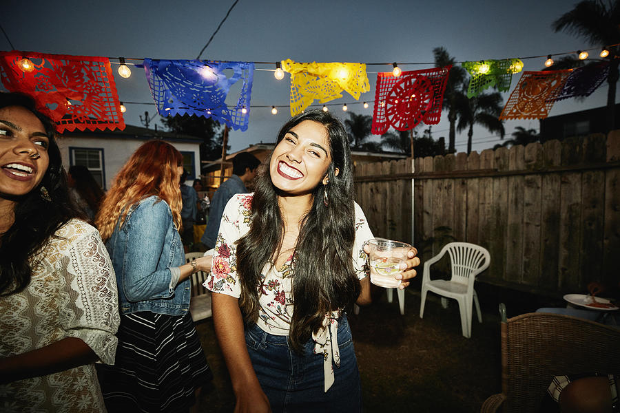 Portrait of laughing woman sharing drinks with friends in backyard on summer evening Photograph by Thomas Barwick