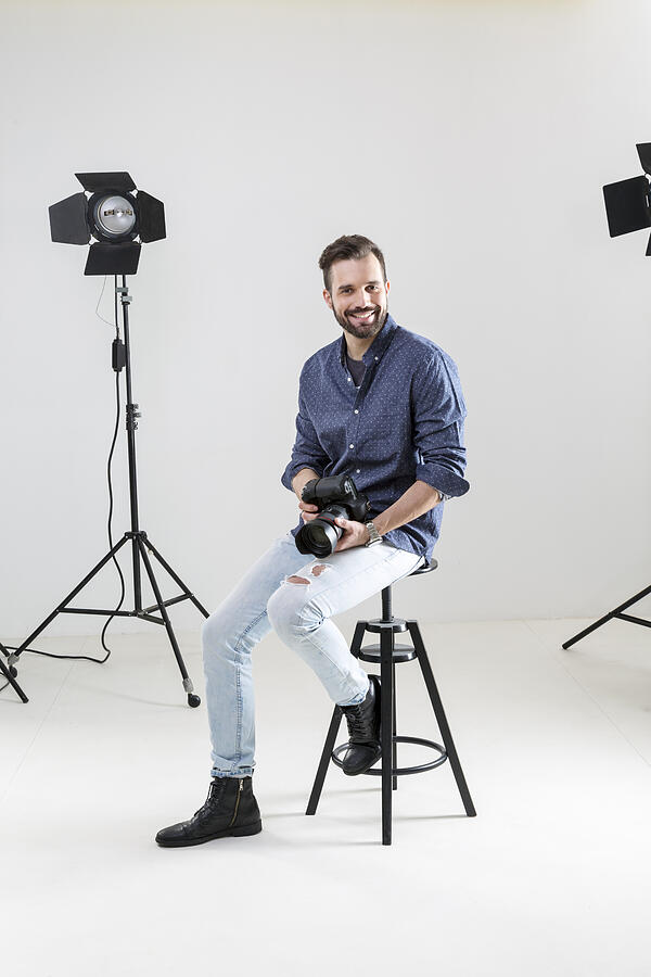 Portrait of male photographer sitting on white background in photographers studio Photograph by Innocenti