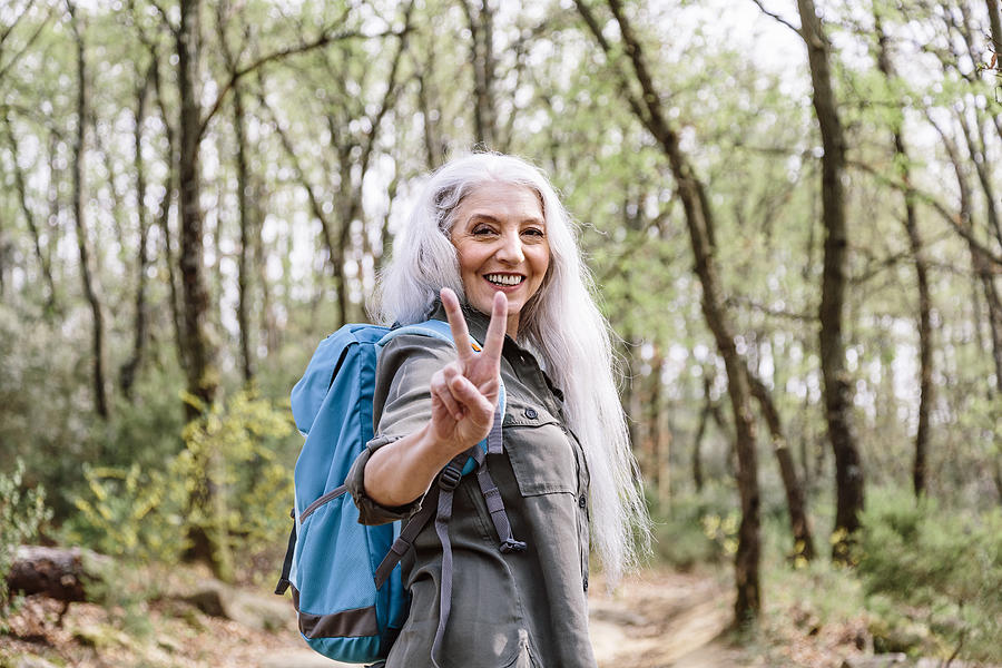 Portrait of mature female backpacker giving peace sign in forest, Scandicci, Tuscany, Italy Photograph by Innocenti