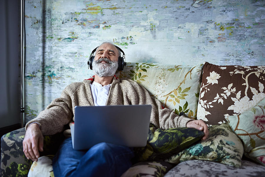Portrait of mature man on sofa smiling and wearing headphones Photograph by 10000 Hours