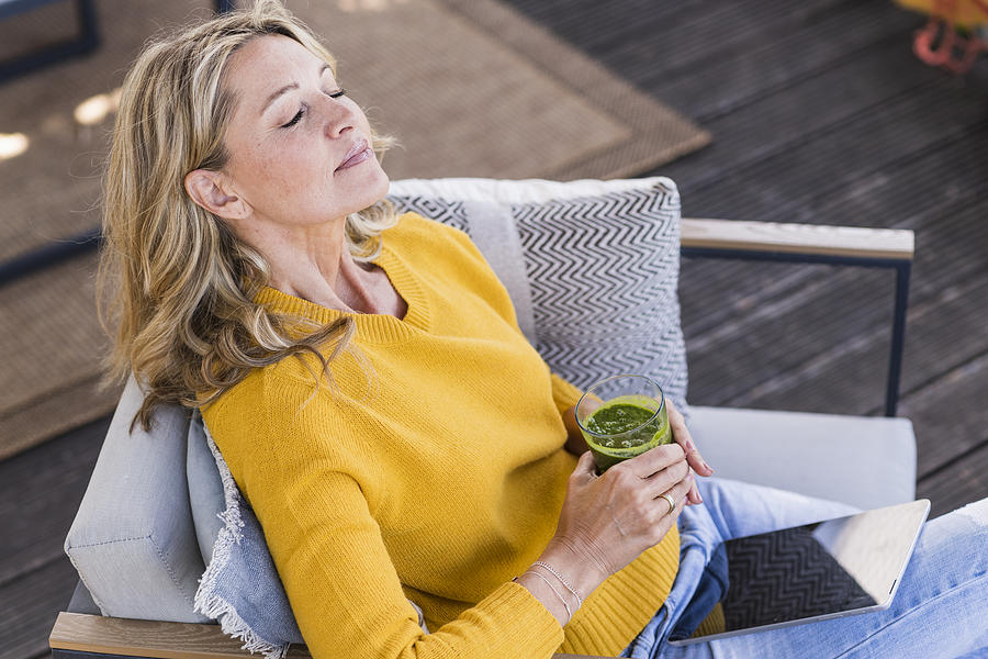 Portrait of mature woman sitting on terrace with digital tablet and glass of smoothie Photograph by Westend61