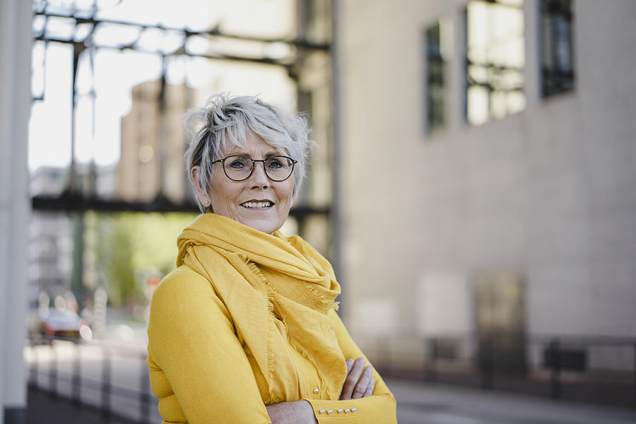 Portrait of mature woman with grey hair wearing glasses and yellow clothes Photograph by Westend61