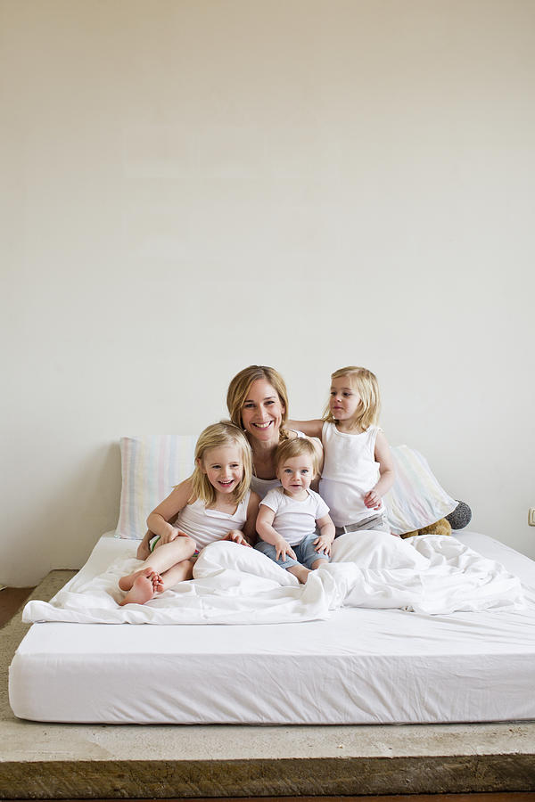 Portrait of mid adult woman in bed with three daughters Photograph by Emely