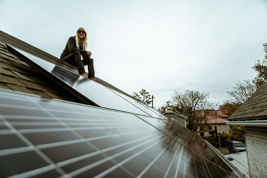 Portrait of mid adult woman sitting on newly solar paneled house roof Photograph by Heshphoto