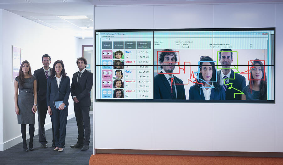 Portrait of office workers standing next to face recognition software system Photograph by Monty Rakusen