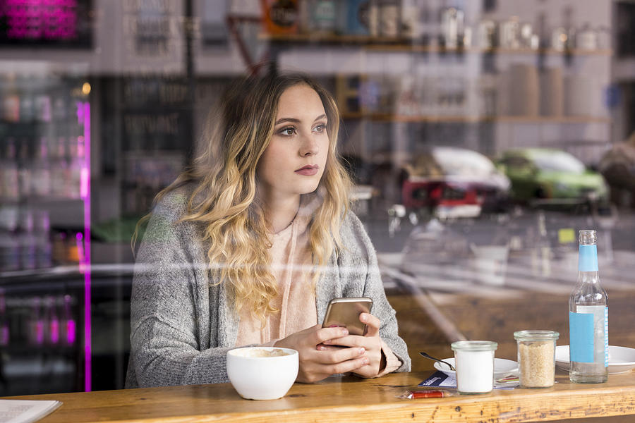 Portrait of pensive young woman in a coffee shop looking through window Photograph by Westend61