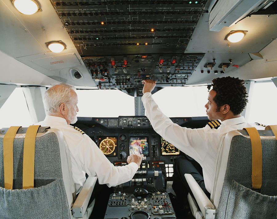 Portrait of Pilots Sitting in the Cockpit, Adjusting the Controls Photograph by Digital Vision.