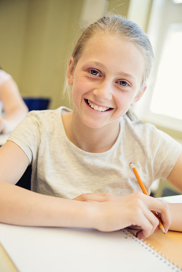 Portrait of preteen girl in classroom, sitting at her desk. Photograph by Martinedoucet