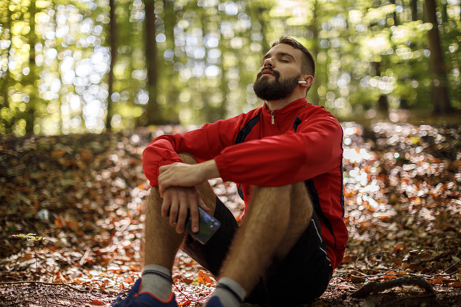 Portrait of relaxed young man with bluetooth headphones in forest Photograph by Damircudic