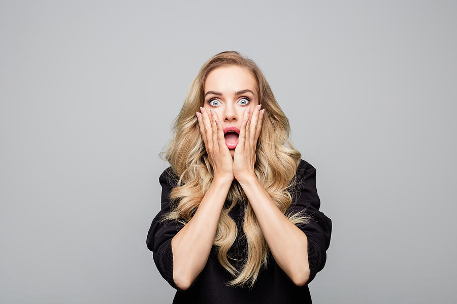 Portrait of shocked young woman with hands on face Photograph by Izusek