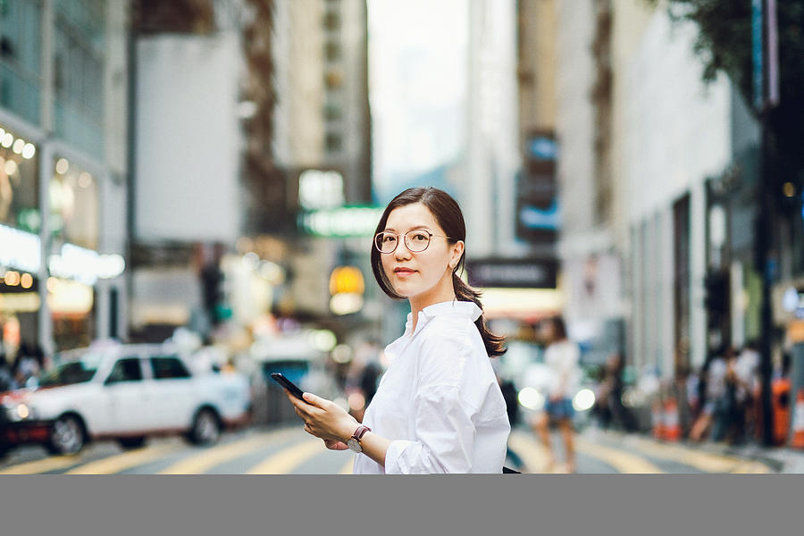 Portrait of smart Asian businesswoman using mobile phone in busy downtown city street Photograph by D3sign