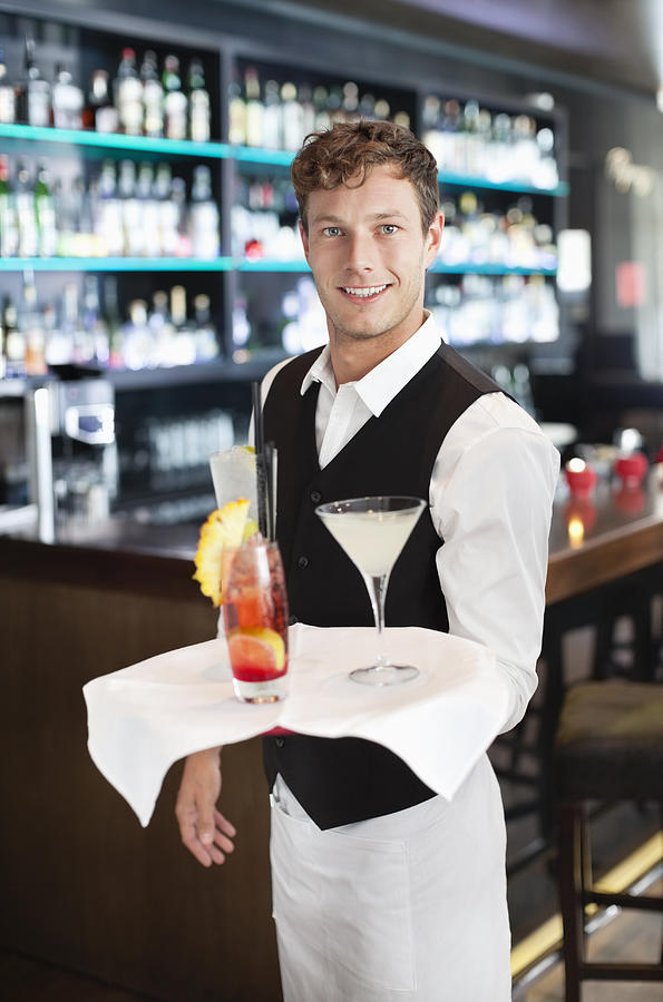 Portrait of smiling bartender holding tray with cocktails in bar Photograph by Chris Ryan