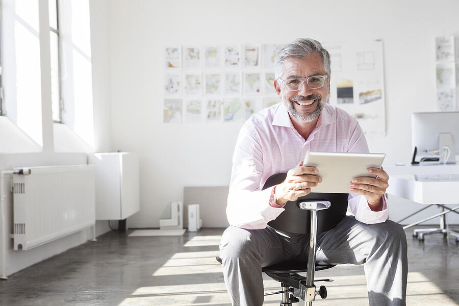 Portrait of smiling businessman with digital tablet in an office Photograph by Westend61